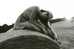 Girl sits on a hay bale in a farm field.